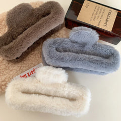 White, brown, and gray faux fur claw clips arranged with a bottle and a book