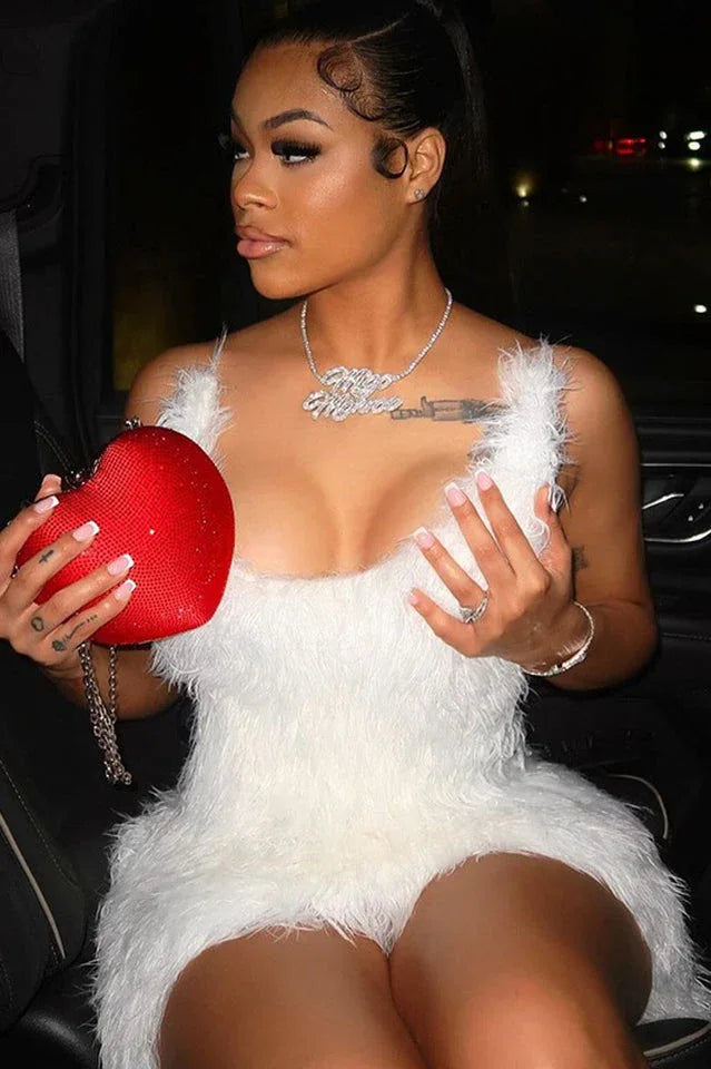 Close-up of a woman in a white fluffy mini dress, holding a red heart-shaped purse.