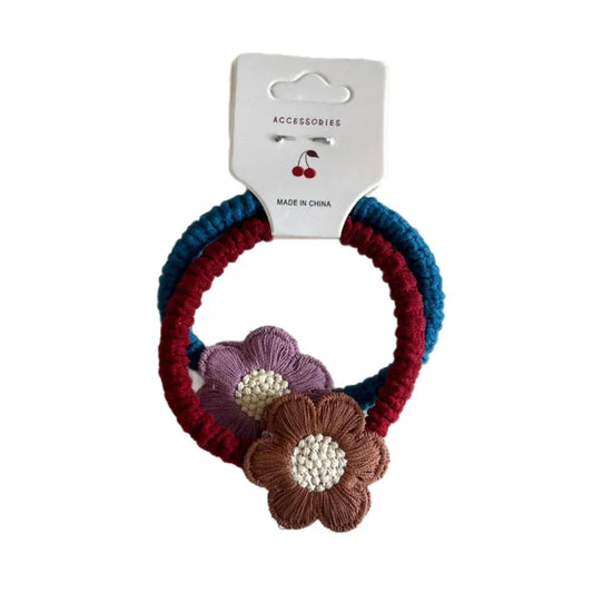A set of two hair ties with braided bands in blue and red, adorned with purple and brown crocheted flowers.