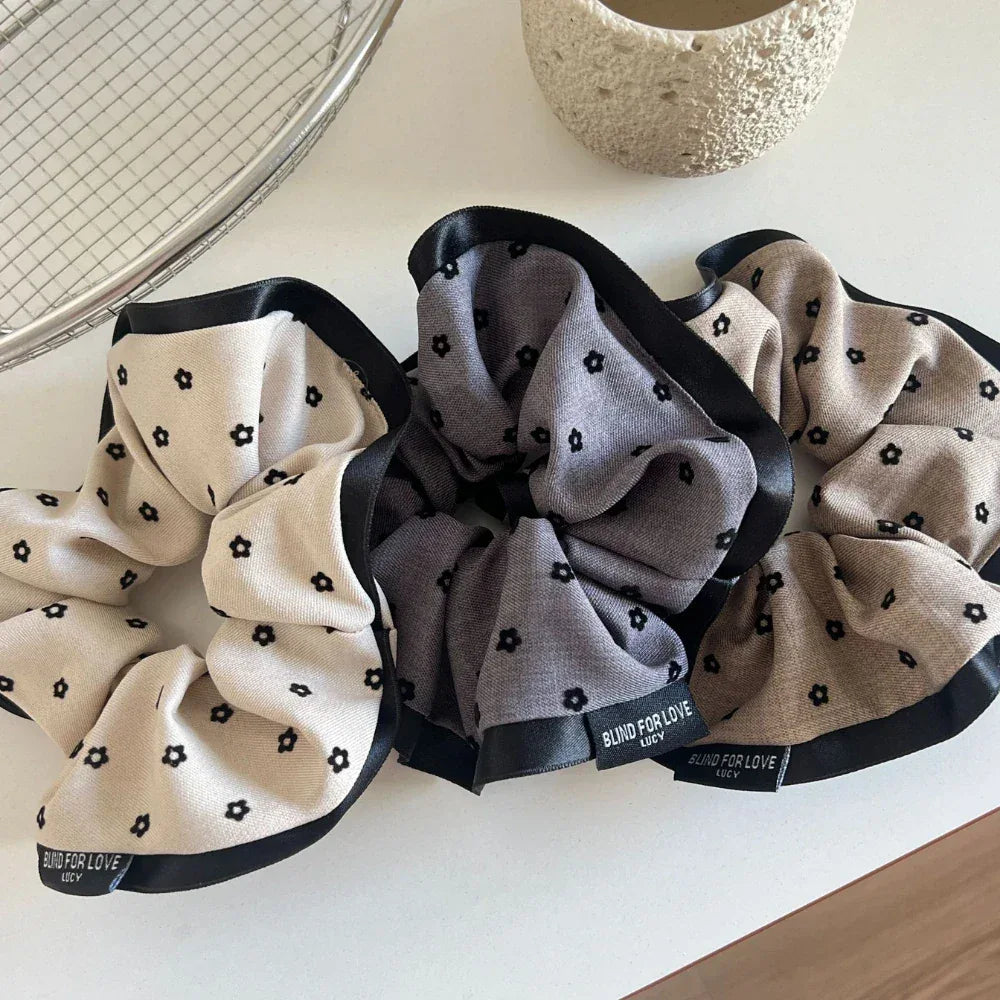 Three scrunchies with floral prints and black satin trims are displayed together on a white surface.