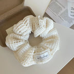 A white crocheted scrunchie with a decorative label on a white surface