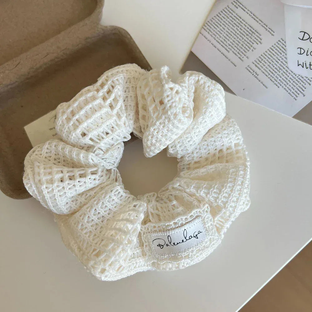 A white crocheted scrunchie with a decorative label on a white surface