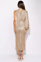 Woman in a gold sequin one-shoulder midi dress with a high neckline and a side slit, shown from the back.