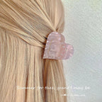 A pink marbled heart-shaped hair clip with faux pearl embellishments, securing a section of blonde hair.