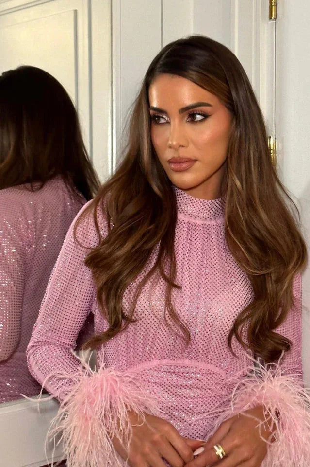 Close-up of a woman's face and chest wearing a pink sparkly dress with feather accents on the sleeves.