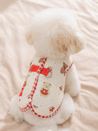 Rear view of a white poodle wearing a cream-colored dog vest with cartoon bears and red gingham trim