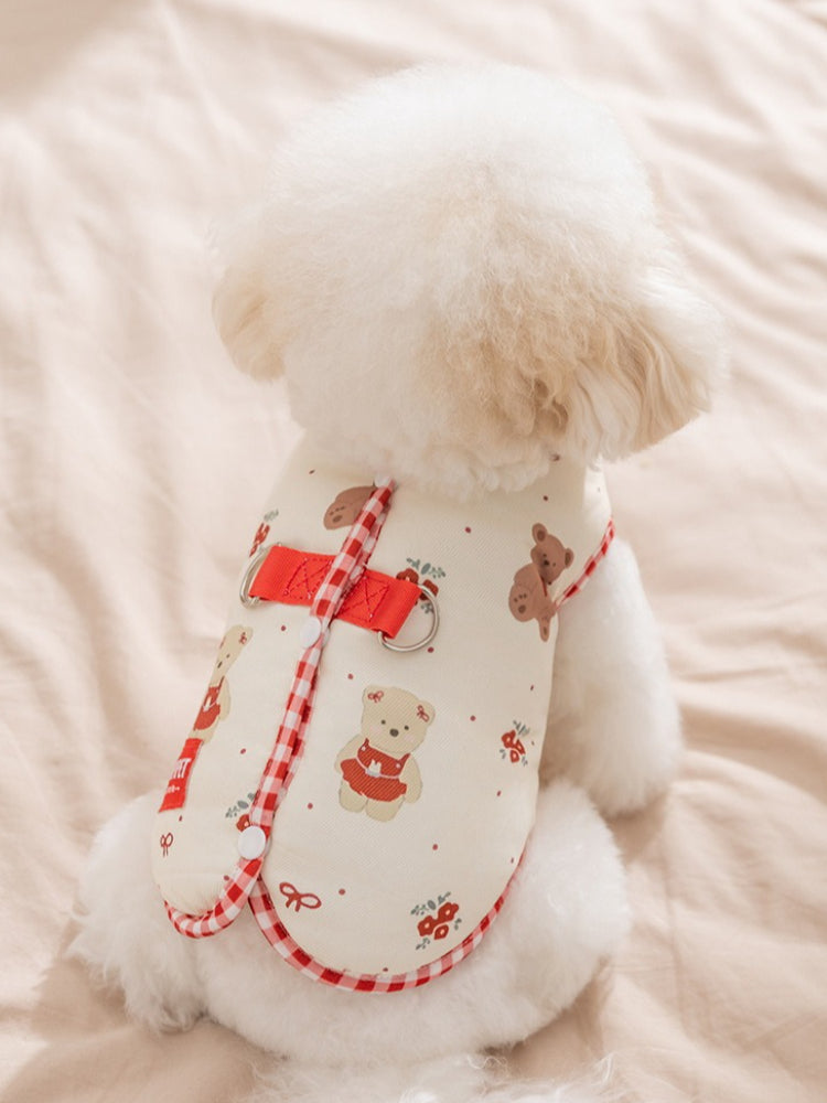 Rear view of a white poodle wearing a cream-colored dog vest with cartoon bears and red gingham trim