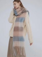 Woman wearing a cream cable knit sweater and a plaid scarf, looking over her shoulder.