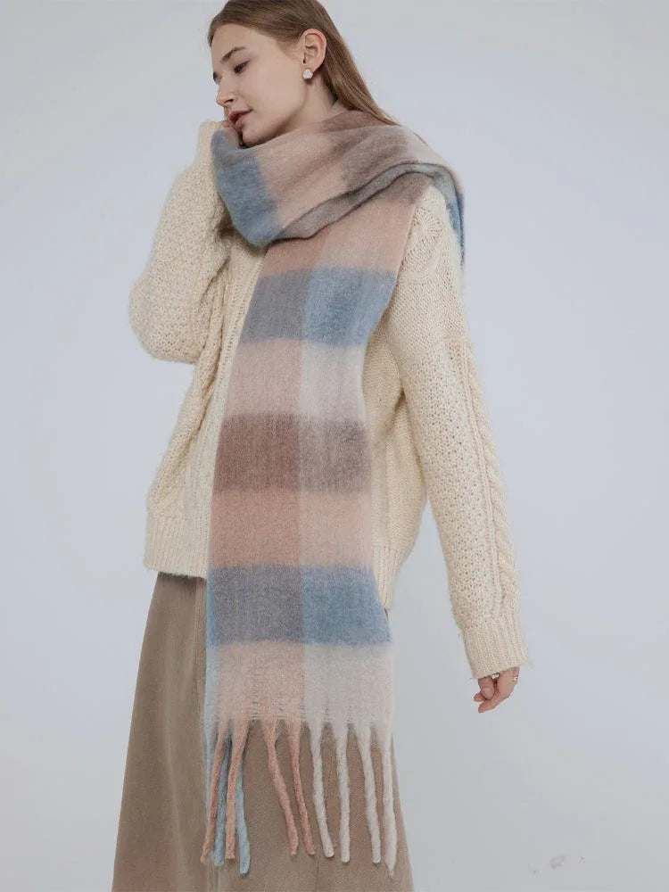 Woman wearing a cream cable knit sweater and a plaid scarf, looking over her shoulder.