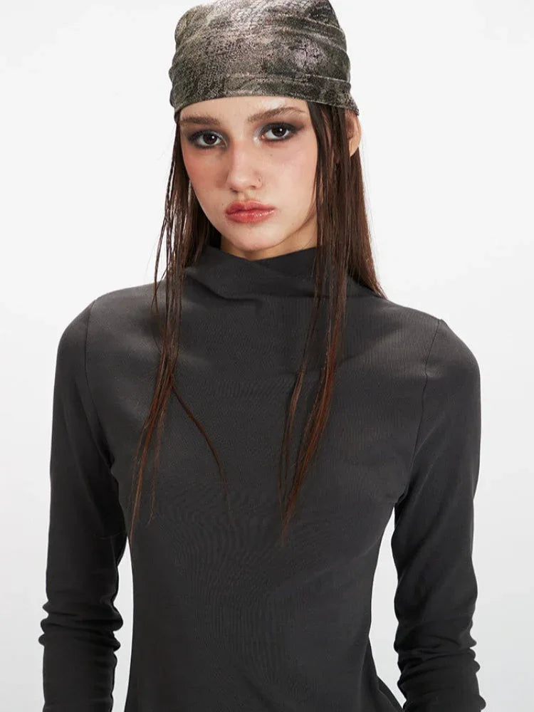 Close-up of a woman's face wearing a grey turtleneck top and a patterned headscarf.