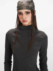 Close-up of a woman's face wearing a grey turtleneck top and a patterned headscarf.