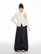 Full body shot of a woman in a cream cable knit cardigan and dark wide-leg jeans, posing with hands on hips