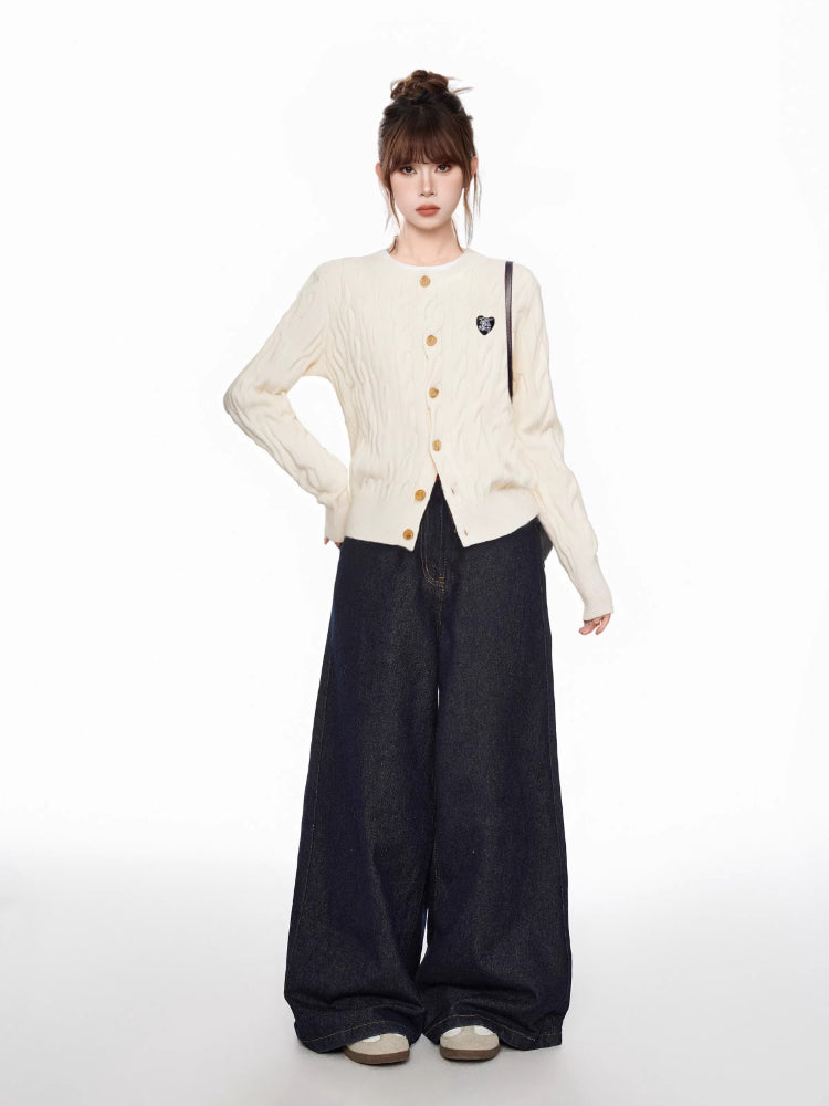 Full body shot of a woman in a cream cable knit cardigan and dark wide-leg jeans, posing with hands on hips