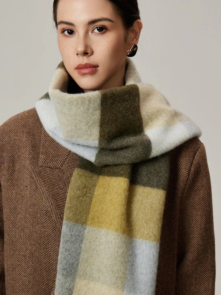 Woman wearing a neutral-toned plaid scarf in shades of green, yellow, and grey over a brown coat.