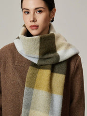 Woman wearing a neutral-toned plaid scarf in shades of green, yellow, and grey over a brown coat.