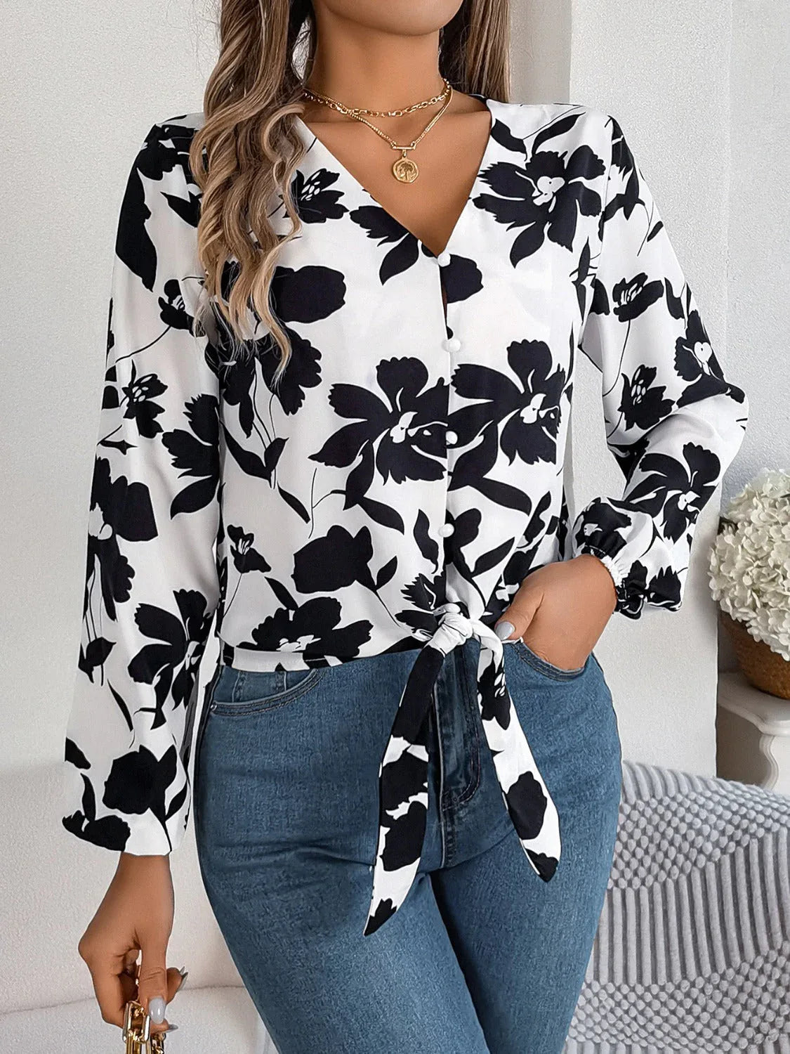 Woman wearing a black and white floral print long sleeve blouse with a front tie detail and blue jeans, front view