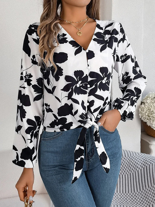 Woman wearing a black and white floral print long sleeve blouse with a front tie detail and blue jeans, front view