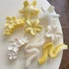 An assortment of yellow and white hair accessories, featuring floral designs, star shapes, and wavy claw clips, spread across a white surface