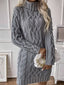 Woman wearing a grey cable knit turtleneck mini dress holding a white handbag.