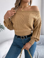Back view of a woman wearing a tan off-the-shoulder cable knit cropped sweater and blue jeans.