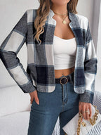 Close-up of a woman wearing a cropped buffalo plaid jacket, white tank top, blue jeans, and accessories, holding a handbag.