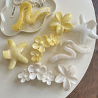 Collection of yellow and white hair accessories including flower shapes, star shapes, and wavy claw clips arranged on a tray and table