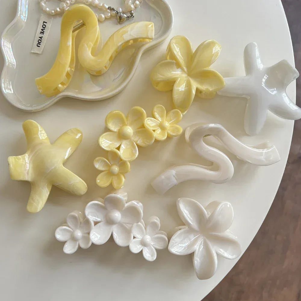 Collection of yellow and white hair accessories including flower shapes, star shapes, and wavy claw clips arranged on a tray and table