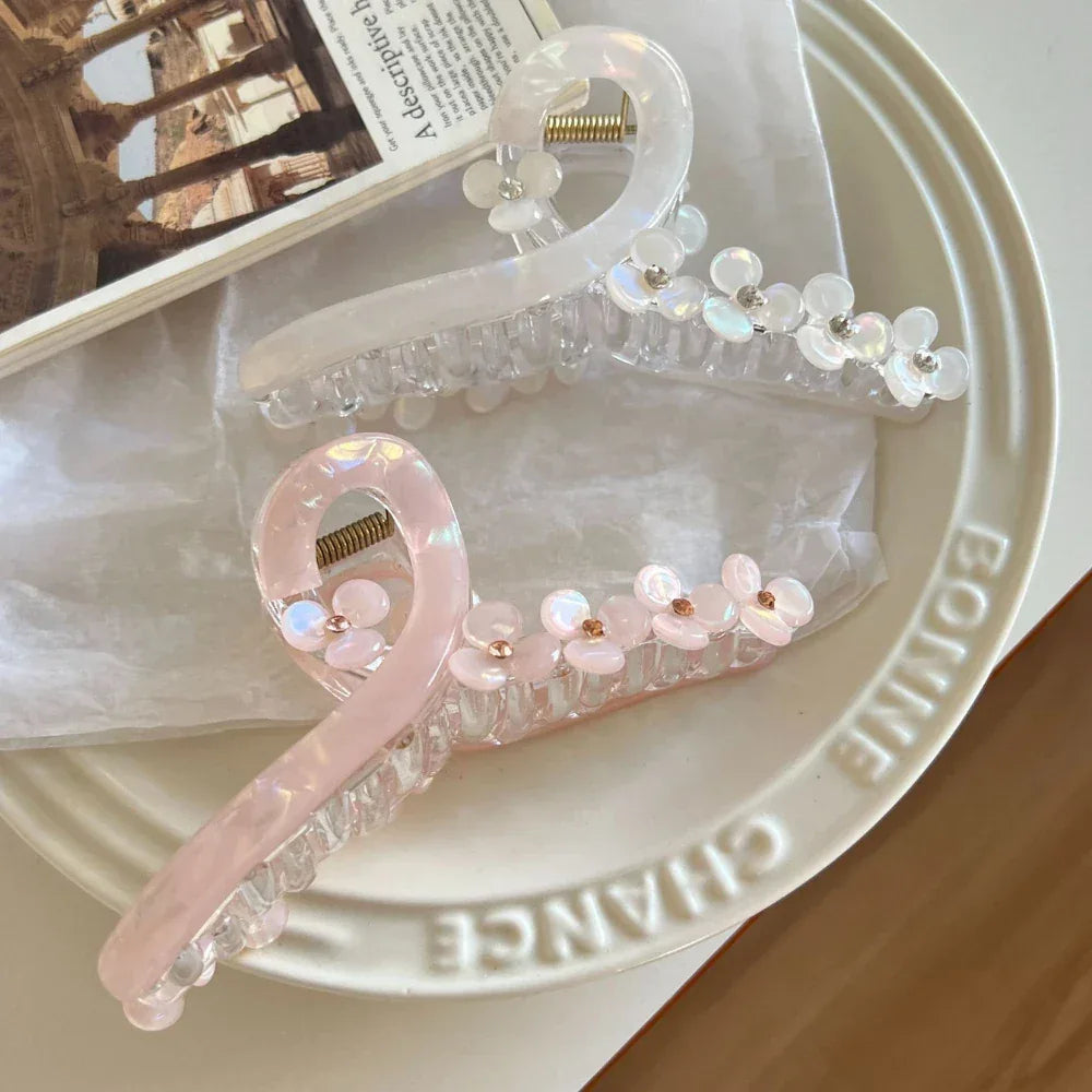 Two translucent claw hair clips, one white and one pink, both decorated with floral details, resting on a plate.