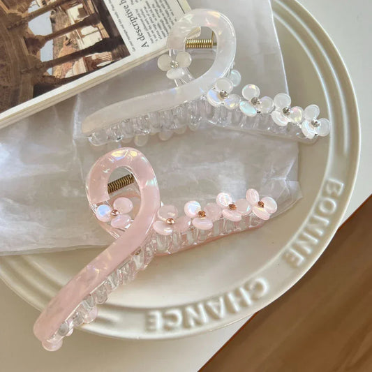 Two translucent claw hair clips, one white and one pink, both decorated with floral details, resting on a plate.