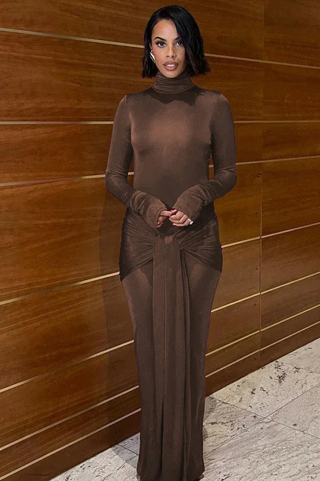 Woman wearing a long-sleeved, brown, mock neck, floor-length dress with a draped knot detail at the waist, posing indoors.