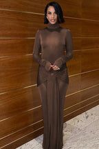 Woman wearing a long-sleeved, brown, mock neck, floor-length dress with a draped knot detail at the waist, posing indoors.
