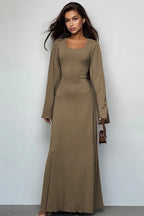 Woman wearing a long-sleeved, ribbed maxi dress with bell sleeves and a square neckline in a taupe color, holding a small brown handbag.