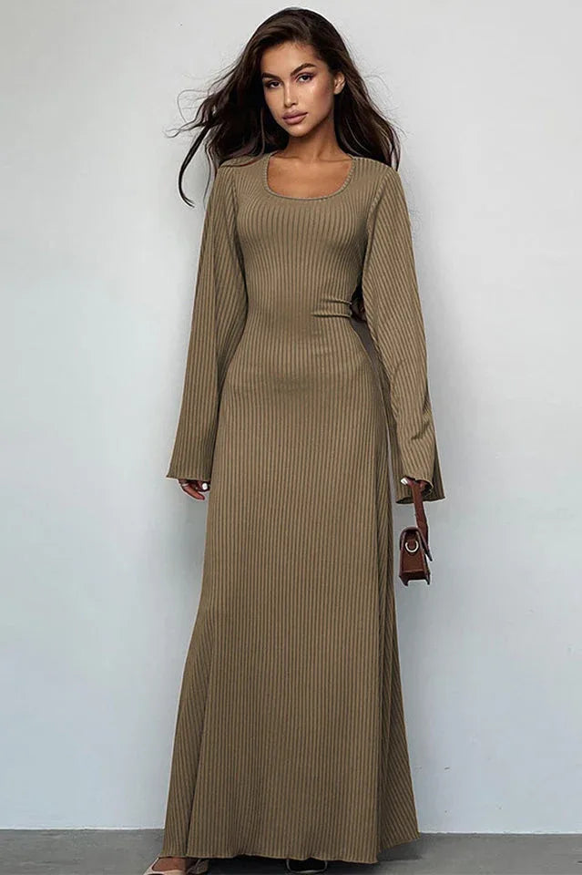Woman wearing a long-sleeved, ribbed maxi dress with bell sleeves and a square neckline in a taupe color, holding a small brown handbag.