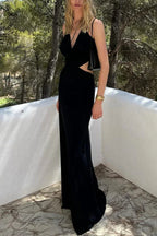 Woman wearing a black, floor-length halter dress with a deep V-neckline and cut-out details on the sides, standing outdoors.