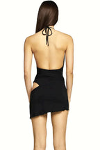 Back view of a woman wearing a black halter neck mini dress with a deep V-neckline and an asymmetrical hemline with a sheer wrap-around skirt detail. The dress features side cut-outs and an open back.