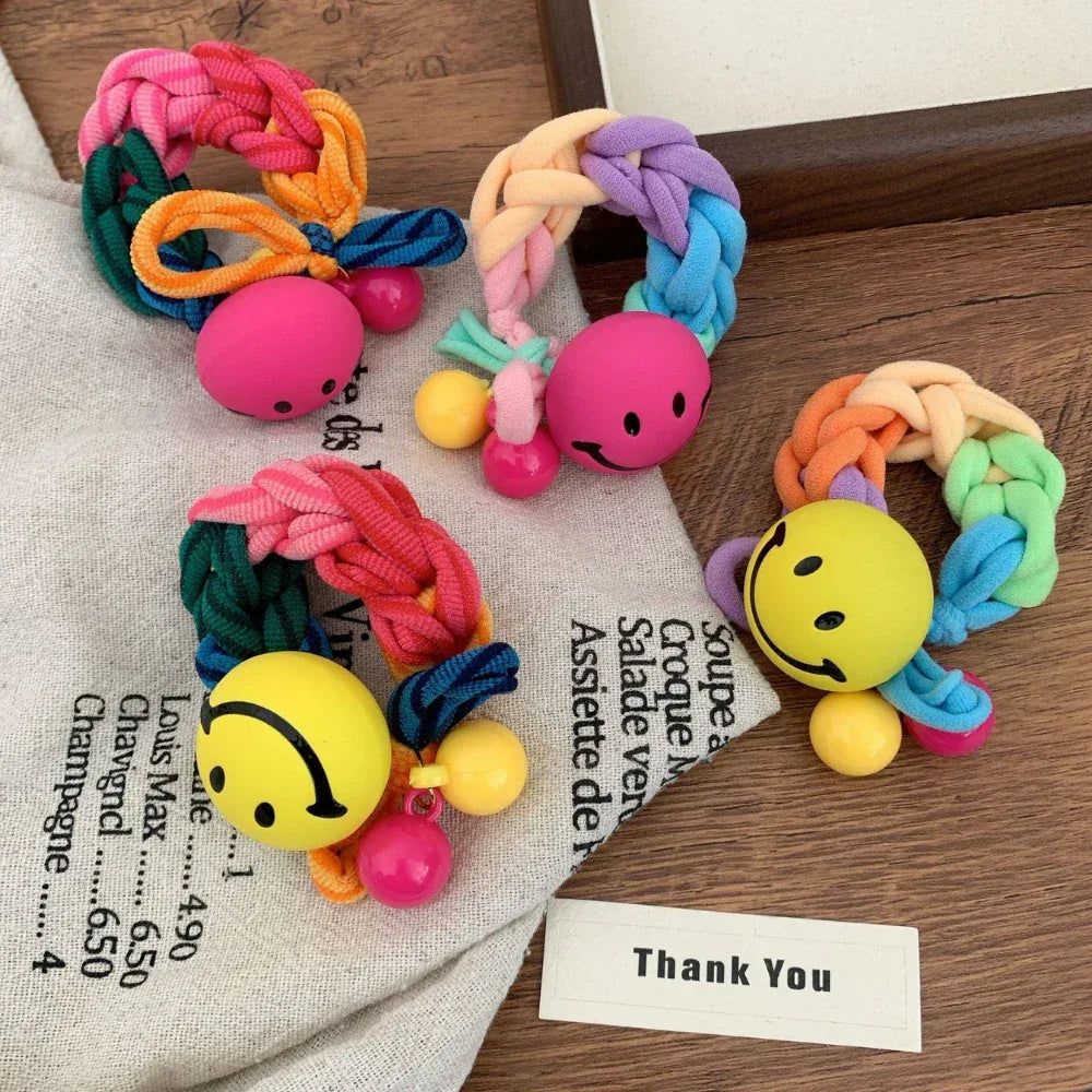 A variety of brightly colored braided hair ties with smiley face charms and bead embellishments, presented in a flat lay arrangement.