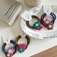 A flat lay of crocheted flower hair ties on a white plate and a table.