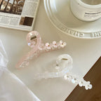 A white and a pink claw hair clip with floral designs are placed on a white surface next to a magazine.