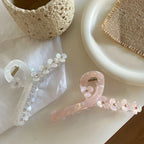 Close-up view of two floral claw hair clips, one white and one pink, on a white surface with decorative items.
