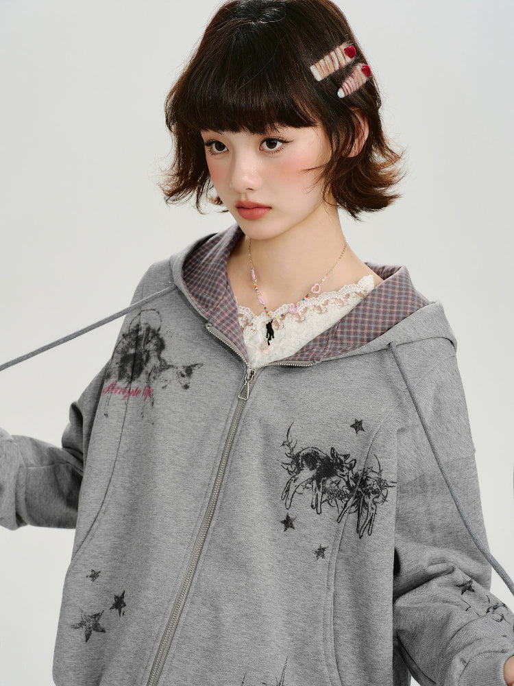 Close-up of a young woman's face and upper body, wearing a grey zip-up hoodie with a graphic print and a lace top.