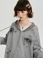 Close-up of a young woman's face and upper body, wearing a grey zip-up hoodie with a graphic print and a lace top.