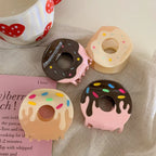 Four donut claw clips in various colors and frosting designs arranged on a surface with a mug and a book.