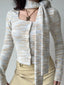 Close-up of a woman wearing a light blue, white, and tan striped knit cardigan with a square neckline and an attached scarf.