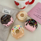 A collection of four donut-shaped claw clips displayed on a linen cloth and next to a mug and a book.