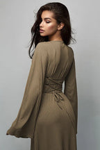 Back view of a woman wearing a long-sleeved, ribbed maxi dress with bell sleeves, showing lace-up detail at the waist in a taupe color.
