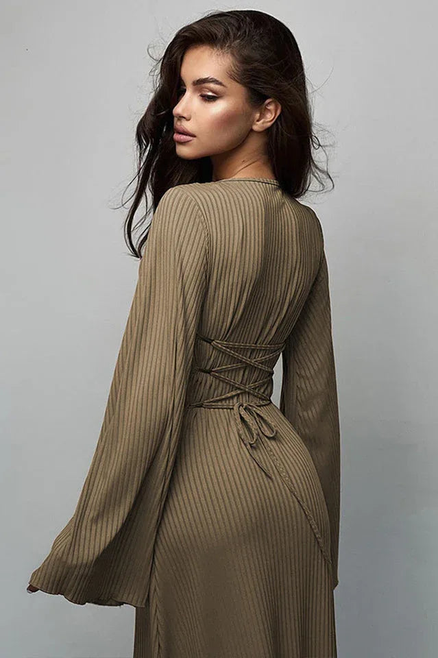 Back view of a woman wearing a long-sleeved, ribbed maxi dress with bell sleeves, showing lace-up detail at the waist in a taupe color.