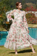 Woman wearing a long, floral print, tiered ruffle chiffon gown with bishop sleeves and a high neck, standing in a garden by a pool.
