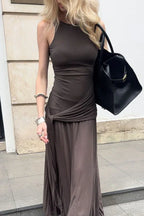 Woman wearing a brown ruched maxi dress with a halter neckline and a black handbag.