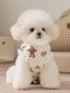 White poodle wearing a light yellow pet vest with a teddy bear print and ruffle trim, sitting down.