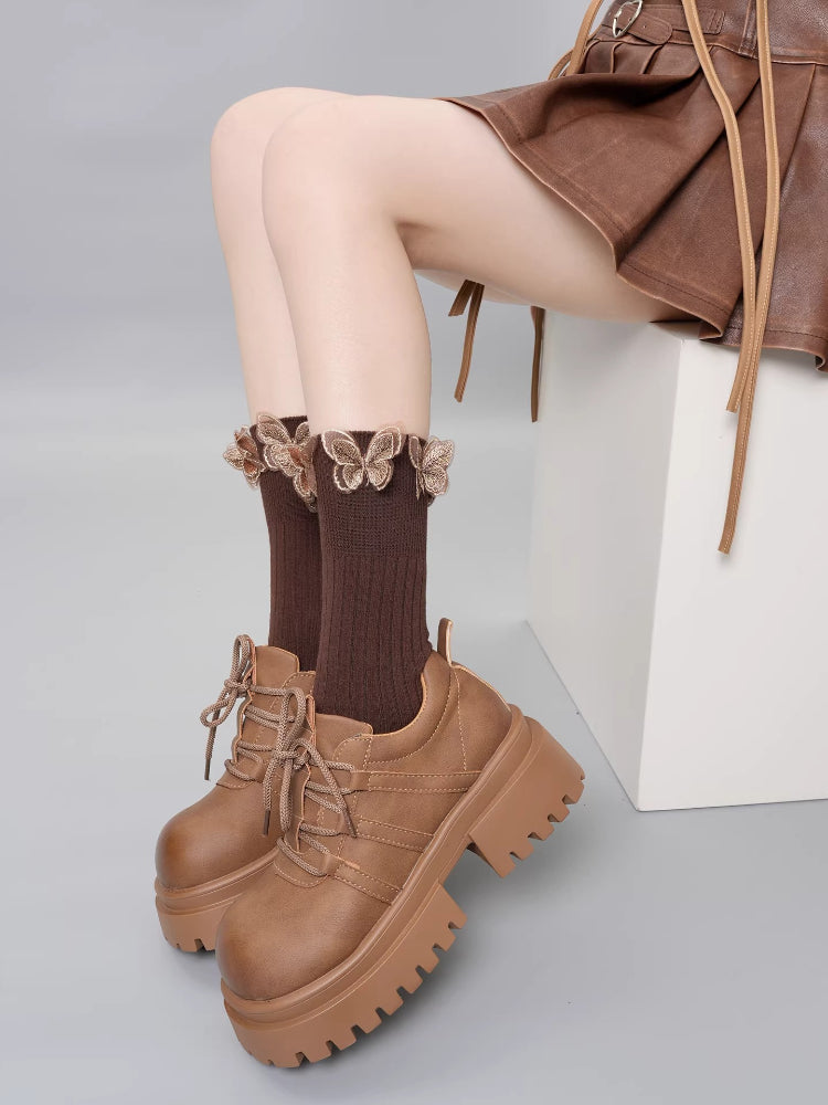 Full shot of brown ribbed socks with ruffled butterfly trim and brown lace-up platform shoes, worn with a brown skirt.